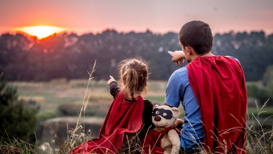 Vader en dochter met superhelden cape wijzen naar de zonsondergang
